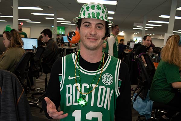 male employee wearing Boston Celtics jersey, bolo hat with shamrocks, and beads.
