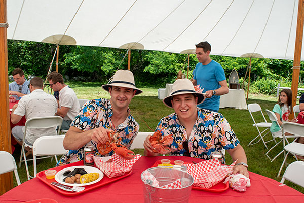 two male employees eating lobster and corn at a company party